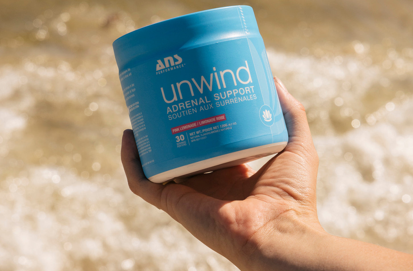 Unwind ANS Performance supplement in a blue container, held in hand, supports stress reduction and energy boost with adaptogens and essential nutrients.