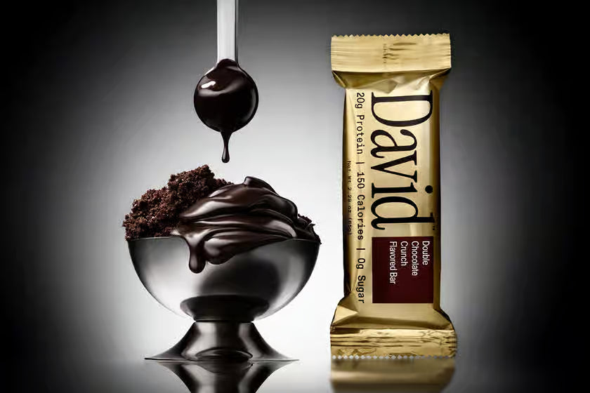 David's Crunch Bar in Double Chocolate Chunk, gold wrapper beside chocolate fudge bowl, highlights 20g protein, low sugar, perfect for post-workout or on-the-go snacking.