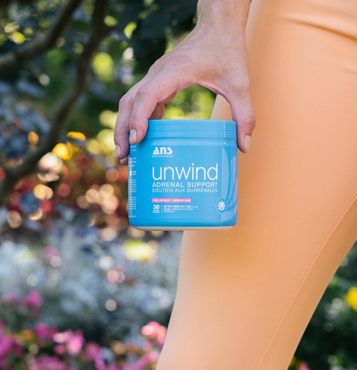 Unwind ANS Performance supplement held by a person, promoting stress reduction and energy boost with KSM-66® Ashwagandha and B Vitamins for adrenal support.